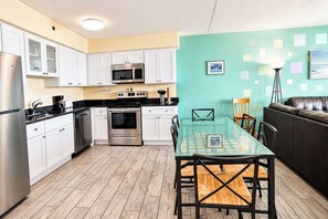 A modern kitchen with white cabinets, stainless steel appliances, and a glass dining table. - Carousel 606 (Ocean City)