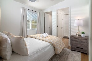 A bedroom with a bed, a nightstand, a lamp, and a door leading to another room. - Historic 1BR Bungalow | Roosevelt Row & Downtown (Phoenix)