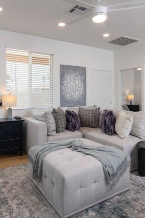 A modern living room with a sectional sofa, a small side table, and a large abstract painting on the wall. - Modern 2BR Casita | Roosevelt Row & Downtown (Phoenix)