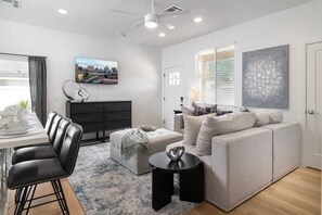Un salon moderne avec un canapé, une table à manger et des chaises, un meuble noir et un tableau représentant un paysage urbain accroché au mur.