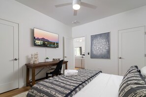 A bedroom with a bed, a desk, a chair, a TV, and artwork on the walls. - Modern 2BR Casita | Roosevelt Row & Downtown (Phoenix)