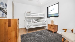 Ein Schlafzimmer mit einem Etagenbett, einer hölzernen Kommode, einem Schreibtisch, einer Lampe und einem gerahmten Bild an der Wand.