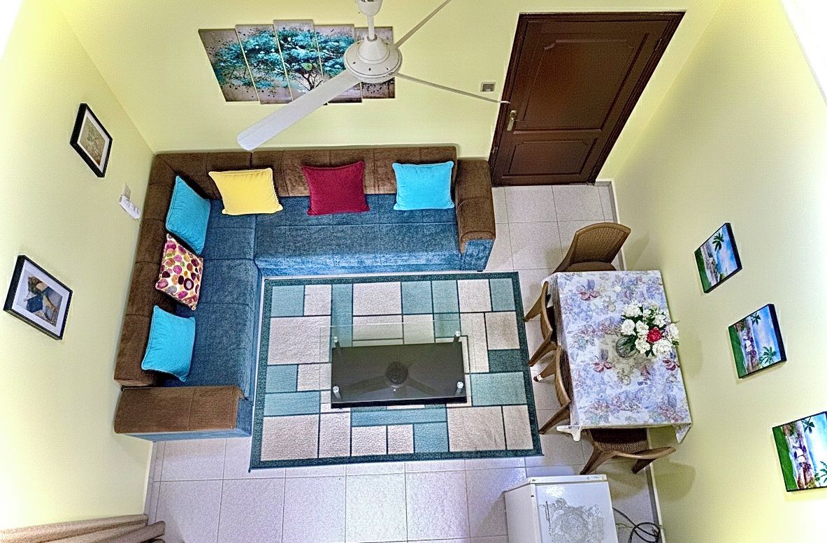 Una stanza con un divano, un tavolino con tovaglia a fiori e una ventola a soffitto.