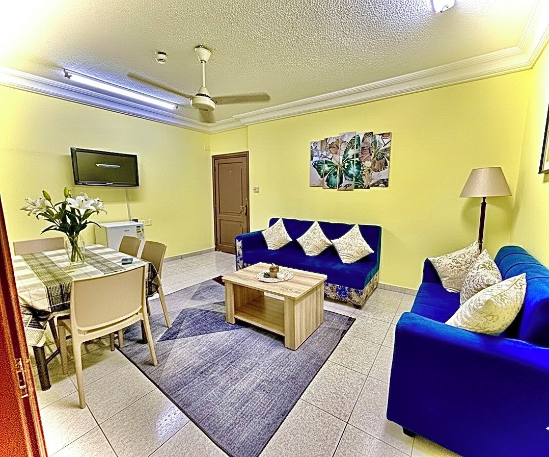 Una sala de estar con un sofá azul, una mesa de centro, un televisor y un comedor con sillas y una mesa.