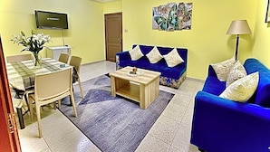 Una sala de estar con un sofá azul, una mesa de centro, un televisor y un comedor con sillas y una mesa.
