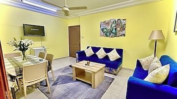 Una sala de estar con un sofá azul, una mesa de centro, un televisor y un comedor con sillas y una mesa.