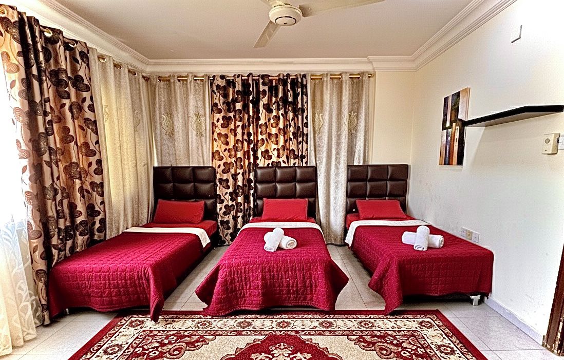 A hotel room with three beds, a ceiling fan, and a patterned rug.