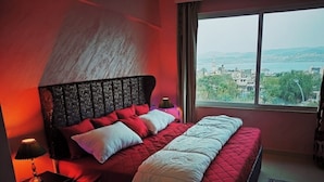Un dormitorio con una cama grande, una mesita de noche, una lámpara y vistas a un paisaje urbano a través de una ventana.