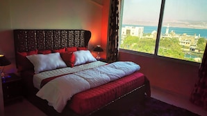 Un dormitorio con una cama grande, una mesita de noche, una lámpara y vistas de la ciudad a través de una ventana.