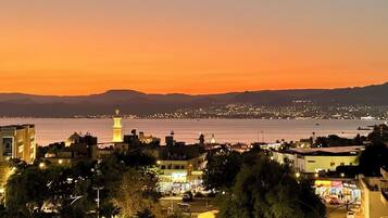 Un paysage urbain côtier au crépuscule, avec une tour imposante, des rues illuminées et une vue sur la mer.