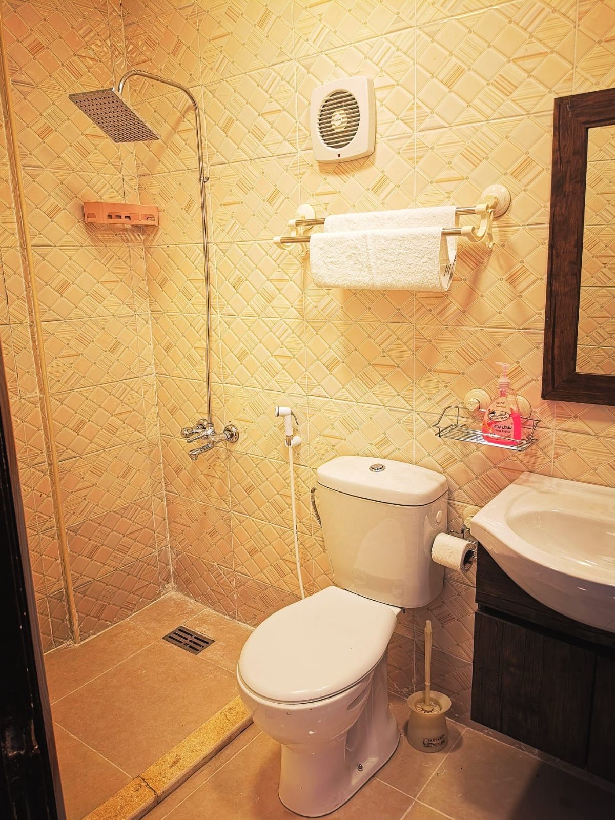 Casa de banho com chuveiro, sanita, lavatório e suporte para toalhas.