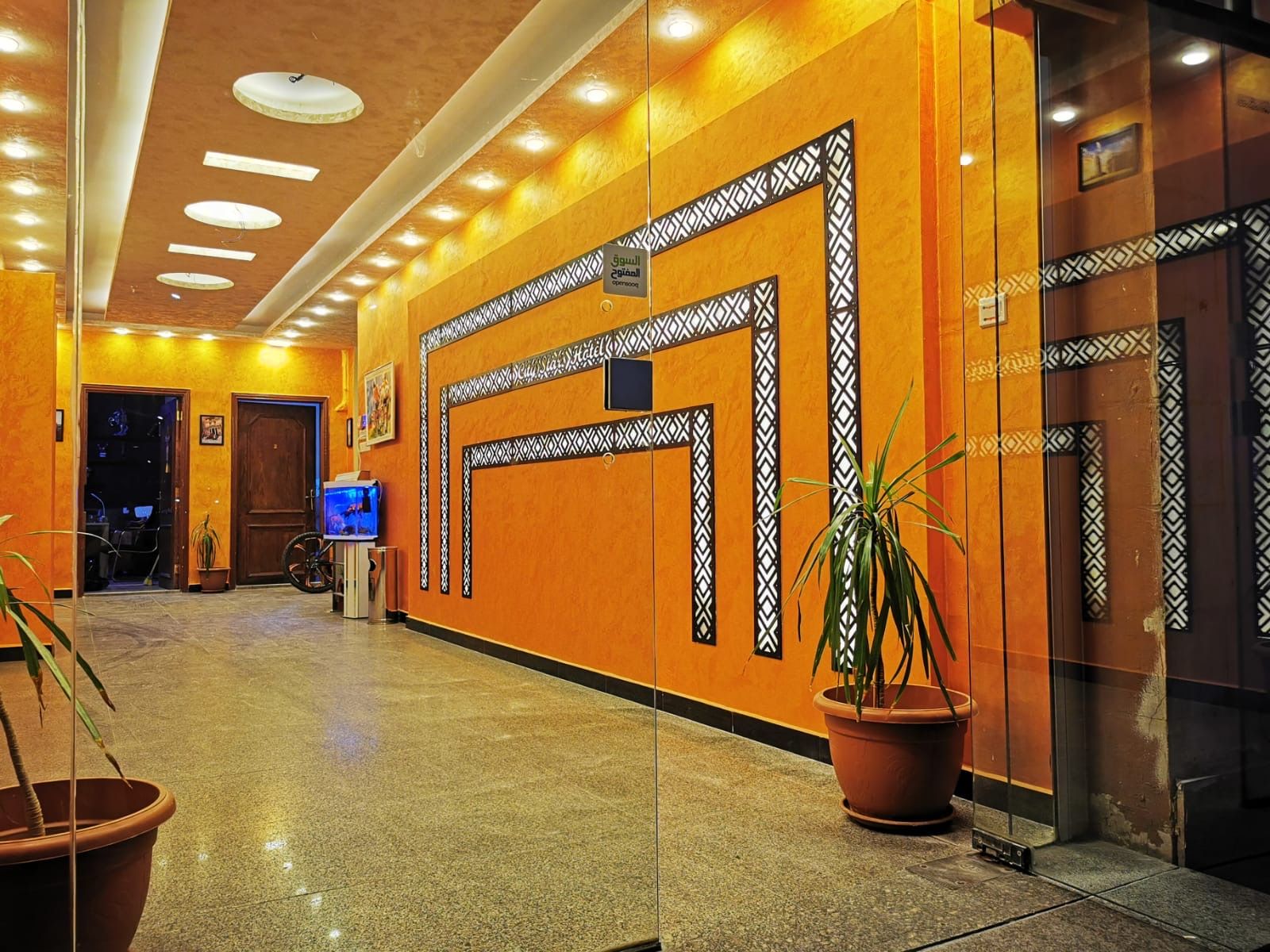 A hotel lobby with a polished floor, decorative wall panels, a television, and potted plants.