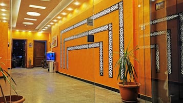 A hotel lobby with a polished floor, decorative wall panels, a television, and potted plants.