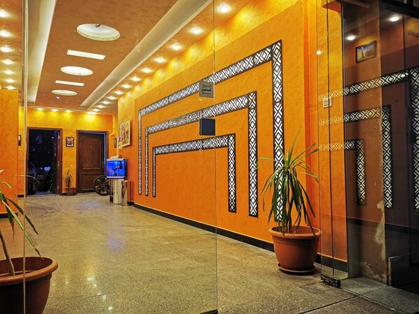 A hotel lobby with a polished floor, decorative wall panels, a television, and potted plants.