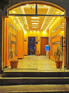 L’entrée d’un hôtel, avec une porte en verre, un comptoir d’accueil et des plantes en pot.