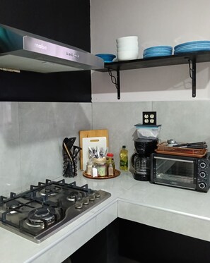 A kitchen with a gas stove, a toaster oven, and a hanging shelf with plates and cups. - Casa Tabor, Lereto Center (Loreto)
