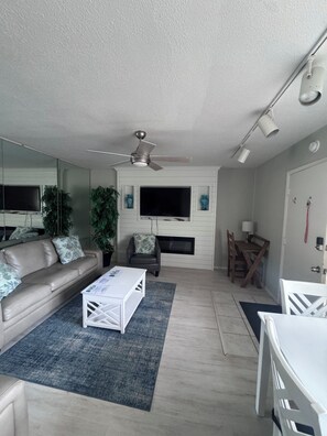 A living room with a sofa, coffee table, TV, fireplace, ceiling fan, and dining area. - 2 Bedroom Siesta Key Condo Private Beach Access, Pool & Tiki Bar (Sarasota)