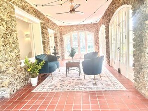 A stone-walled room with a tiled floor, two blue armchairs, a small table, and a potted plant. - The Cobblestone Estate - Historic Downtown Ocala! (Ocala)