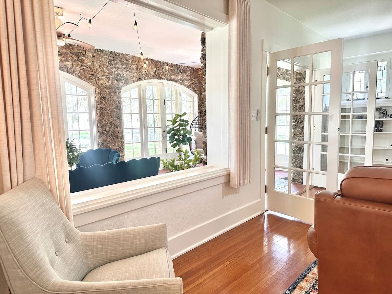 A room with a stone wall, a large window, a blue chair, a brown leather chair, and a wooden floor.