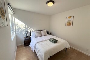 Ein Schlafzimmer mit Bett, Nachttisch, Lampe und einem Kunstwerk an der Wand.