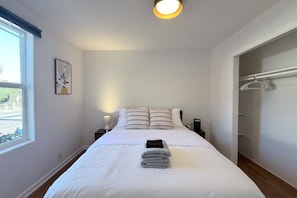 A hotel room with a bed, bedside table, lamp, and a window with a view. - 714 Awesome 2-bedroom house in San Mateo perfect for your getaway (San Mateo)