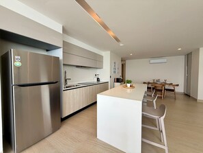 Een moderne keuken met een roestvrijstalen koelkast, een centraal eiland met zitplaatsen en een eethoek met houten meubilair.