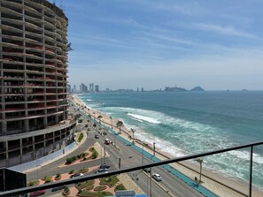 A coastal cityscape with a beachfront road, a large building under construction, and a distant city skyline. - Luxury Oceanfront Apartment: Elegance and Relaxation byGPS (Mazatlán)