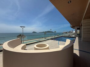 A modern pool area with a curved seating arrangement overlooking a beach and ocean. - Luxury Oceanfront Apartment: Elegance and Relaxation byGPS (Mazatlán)
