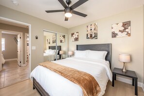 Una camera d'albergo con un letto, lampade sui comodini, una ventola a soffitto e opere d'arte alle pareti.