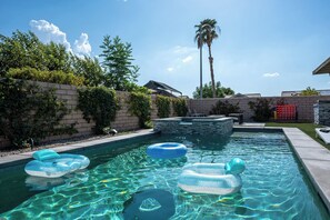 Una piscina con acqua cristallina, circondata da un muro in mattoni e dalla vegetazione, con una palma sullo sfondo.