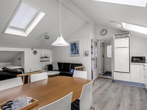 A modern kitchen with a dining area, a black leather sofa, a wooden dining table, and a white refrigerator. - "Dior" - 800m from the sea by Interhome (Hejls)