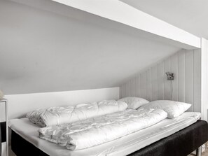A single bed with a white duvet and pillows in a room with white walls and a sloped ceiling. - "Dior" - 800m from the sea by Interhome (Hejls)