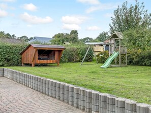 A fenced backyard with a wooden playhouse, a slide, and a swing set. - "Dior" - 800m from the sea by Interhome (Hejls)
