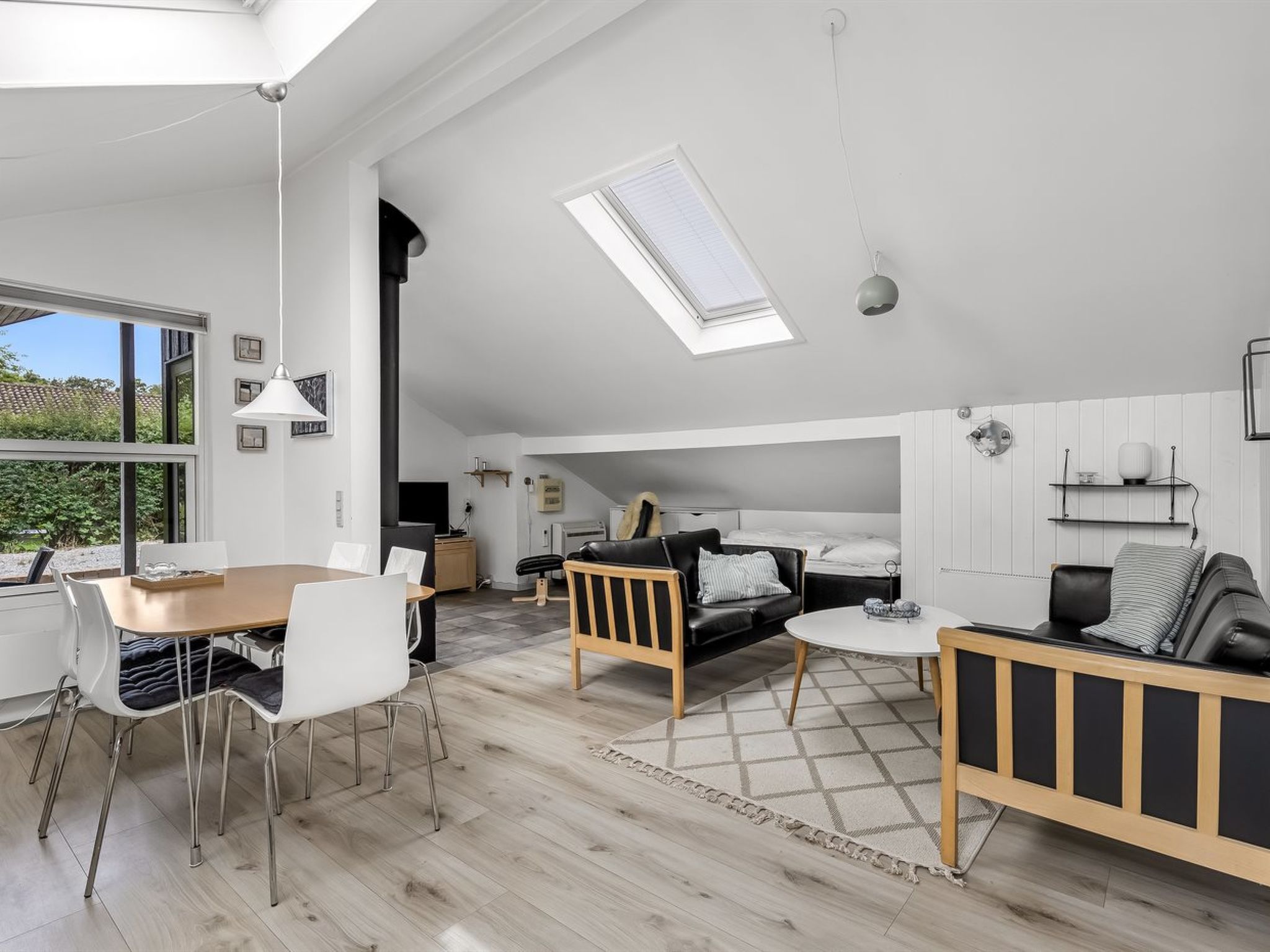 A spacious living area with a dining table, sofas, and a high ceiling with skylights.