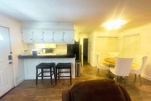 A compact kitchen with white cabinets, a microwave, and a small dining area with two chairs and a table. - Bourbon & Lace Retreat (Texanna)