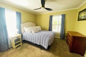 Ein Schlafzimmer mit Bett, Nachttisch, Kommode und Deckenventilator.