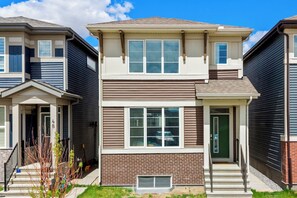 A two-story townhouse with a brick facade, large windows, and a front porch. - Modern 3BR Home | Sleeps 6 | Free Parking & BBQ (Calgary)