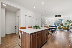 A modern kitchen with a central island, wooden cabinets, and a dining area with chairs and a table. - Modern 3BR Home | Sleeps 6 | Free Parking & BBQ (Calgary)