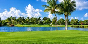 Ein Golfplatz mit einem Wasserhindernis, Palmen und blauem Himmel.