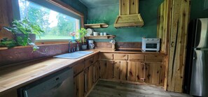 A kitchen with wooden cabinets, a sink, a coffee maker, and a small oven. - Starry Pines Cabin: A handmade cozy cabin-near waterfall, dogs welcome (Blountsville)