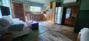 Un salon chaleureux avec un canapé, une table basse et un coin cuisine doté de meubles et d’appareils électroménagers en bois.