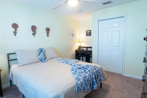 A bedroom with a bed, a nightstand, a lamp, and a door. - Seahorse House - Coastal Charm, Community Pool & Beach Days (Panama City Beach)