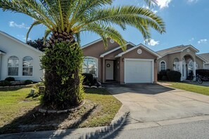 A residential house with a garage, a driveway, and a palm tree. - Seahorse House - Coastal Charm, Community Pool & Beach Days (Panama City Beach)