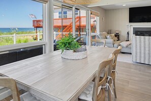 Ein geräumiges Wohnzimmer mit großem Fenster mit Meerblick, ein Essbereich mit Holztisch und eine Küchenzeile mit Fernseher.