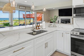 Une cuisine moderne avec des meubles blancs, une cuisinière en acier inoxydable et une grande fenêtre donnant sur un paysage magnifique.