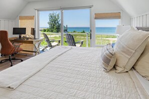 Une chambre avec un grand lit, un bureau avec un ordinateur et une vue sur l’océan.