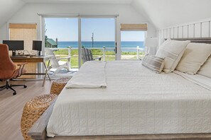 Ein Schlafzimmer mit einem großen Bett, einem Schreibtisch mit Computer und Blick auf den Ozean.
