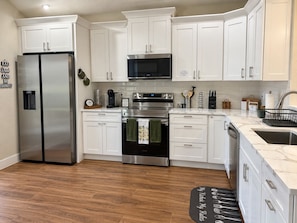 A modern kitchen with white cabinets, stainless steel appliances, and a wooden floor. -  The Chosen Experience (Palm Coast)