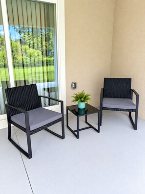 A balcony with two wicker chairs and a small table, a potted plant, and a view of greenery. -  The Chosen Experience (Palm Coast)