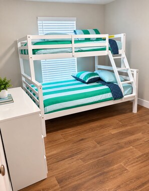 A bunk bed with a desk and drawers, a window with blinds, and a wooden floor. -  The Chosen Experience (Palm Coast)